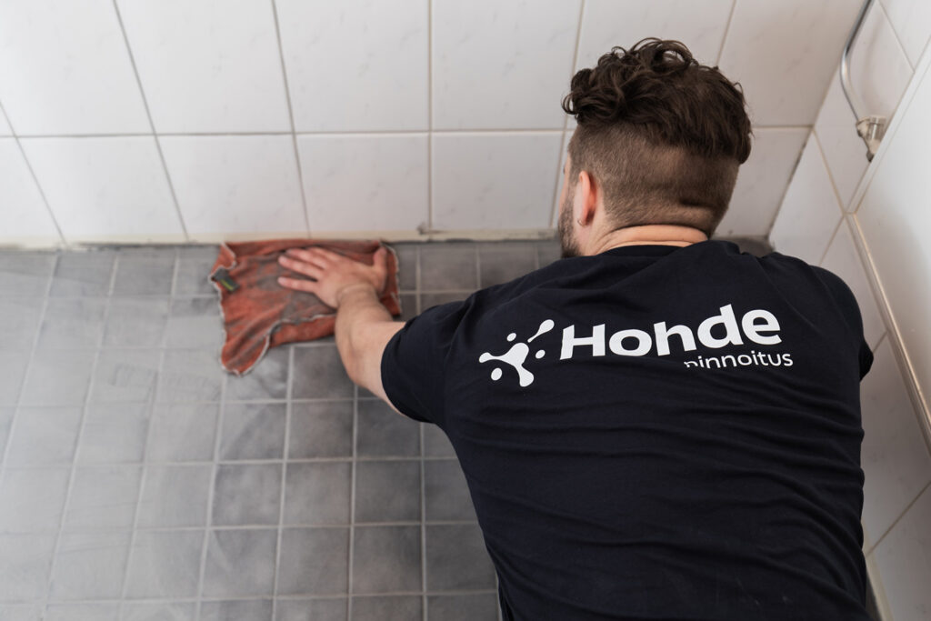 Asentaja tummassa Hohdepinnoitus-paidassa pyyhkii juuri uusittuja laattasaumoja