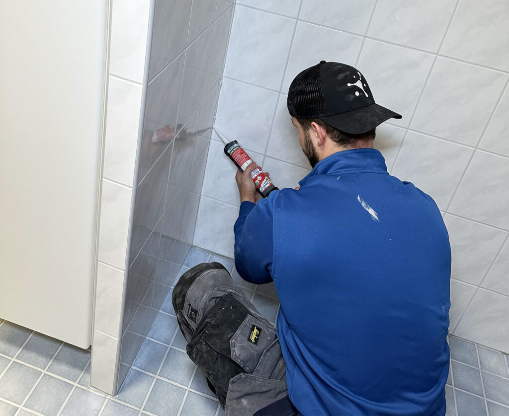 Hohteen asentaja pursottaa silikonia kylpyhuoneen seinään