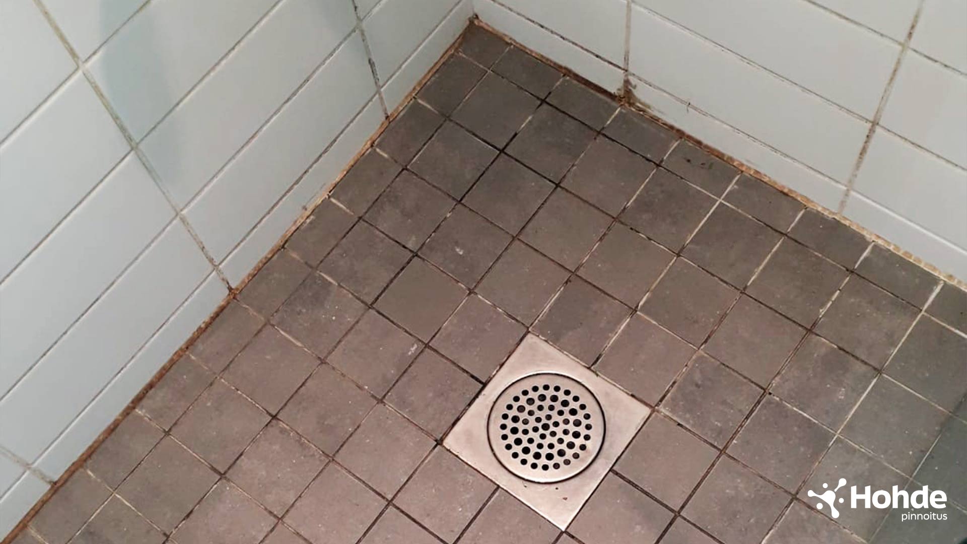Kylpuhuoneen nurkka, jossa lika ja homeet ovat värjänenet laattasaumat tummiksi.